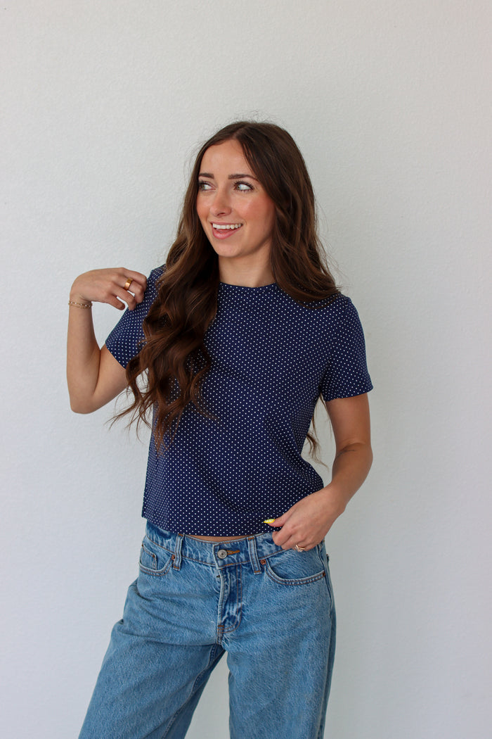 Woman wearing a blue polka dot shirt and jeans against a white background